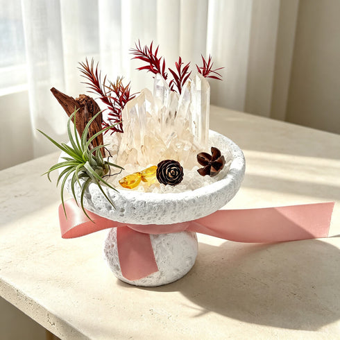 White stone planter with clear quartz cluster, red stems and pinecone accents, pink ribbon