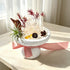 White stone planter with clear quartz cluster, red stems and pinecone accents, pink ribbon
