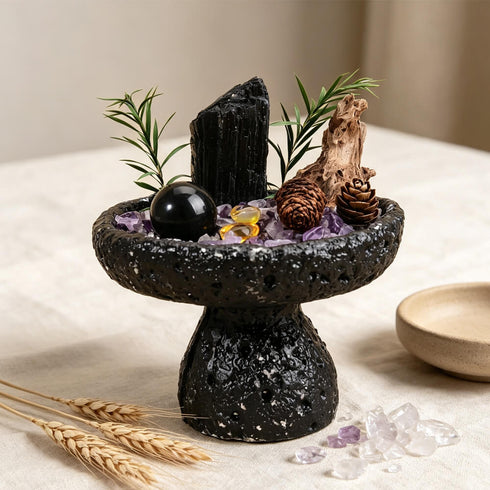 Decorative crystal bowl set with black stone, purple crystal pieces, black sphere, and pine sprigs