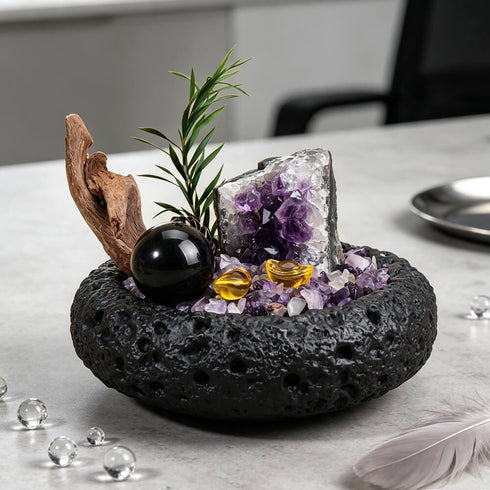 Decorative crystal bowl with amethyst cluster, black sphere, gold accents, and green pine sprigs
