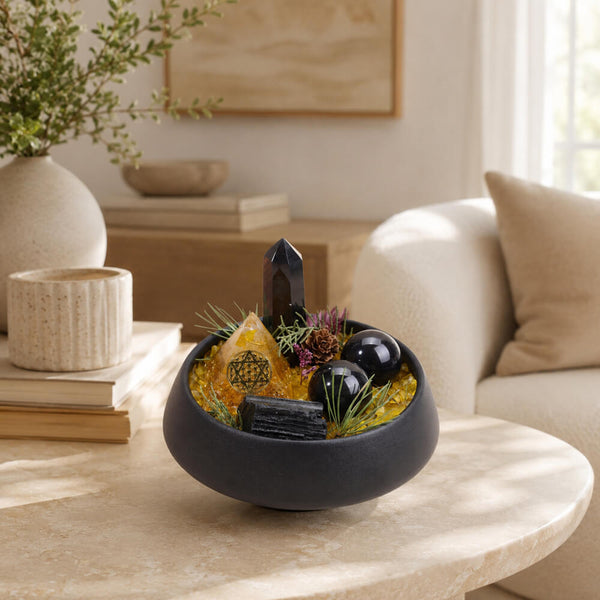 Dark round bowl with black crystal point, gold pyramid, black orbs, and green sprigs