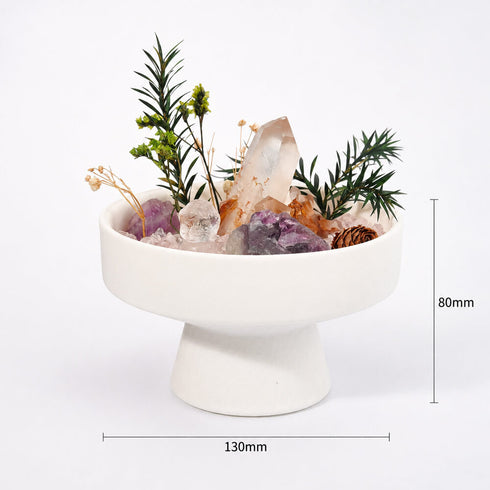 White pedestal bowl centerpiece with green sprigs and assorted pink and purple crystals