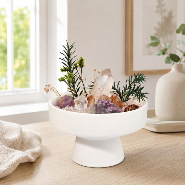 White pedestal crystal garden arrangement with green sprigs and assorted clear, pink, purple rocks