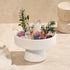 White crystal bowl centerpiece with green sprigs, pinecones, and pink and purple crystal pieces