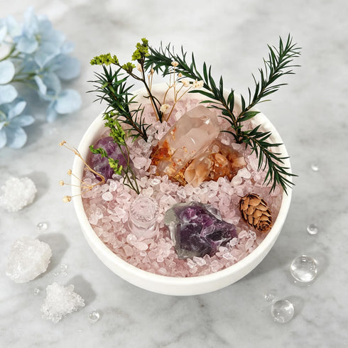 White bowl with rose-colored crystal bed, green sprigs, and clear crystal points