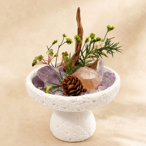 Natural crystal bonsai centerpiece on white pedestal with purple crystal, clear stone, and pinecone