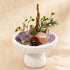 Natural crystal bonsai centerpiece on white pedestal with purple crystal, clear stone, and pinecone